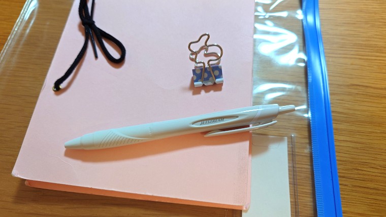 連絡帳、ペン、クリップ、スライダー式ファイルが写っている